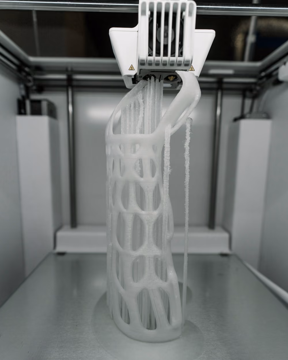 Impresora 3D fabricando una pieza alta de celosía en filamento blanco