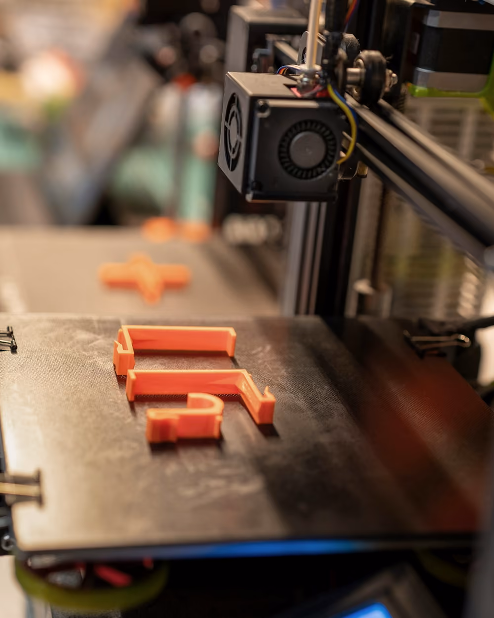 Piezas naranjas recién impresas sobre la cama de una impresora 3D de taller