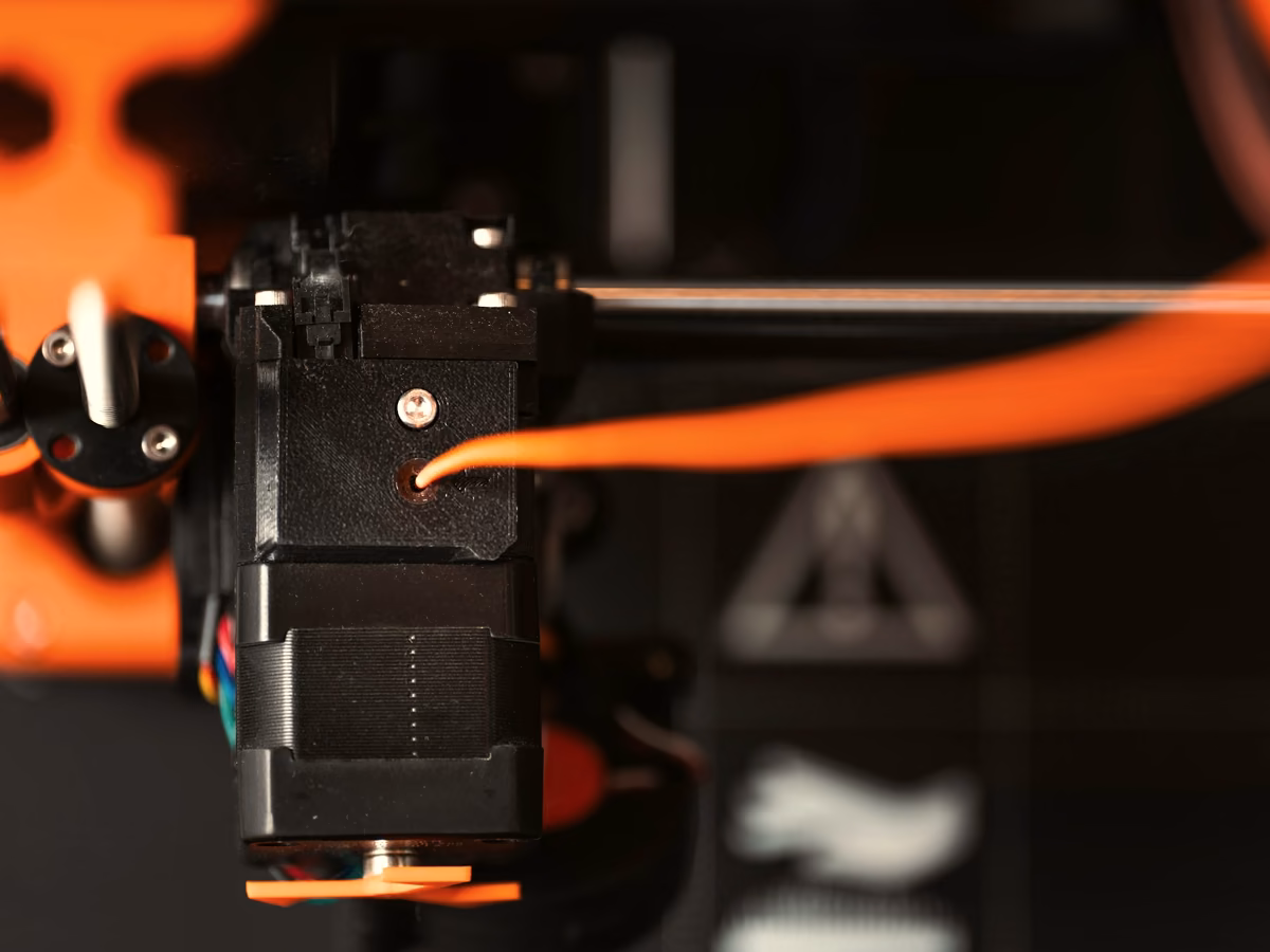 Extrusor de una impresora 3D depositando filamento naranja